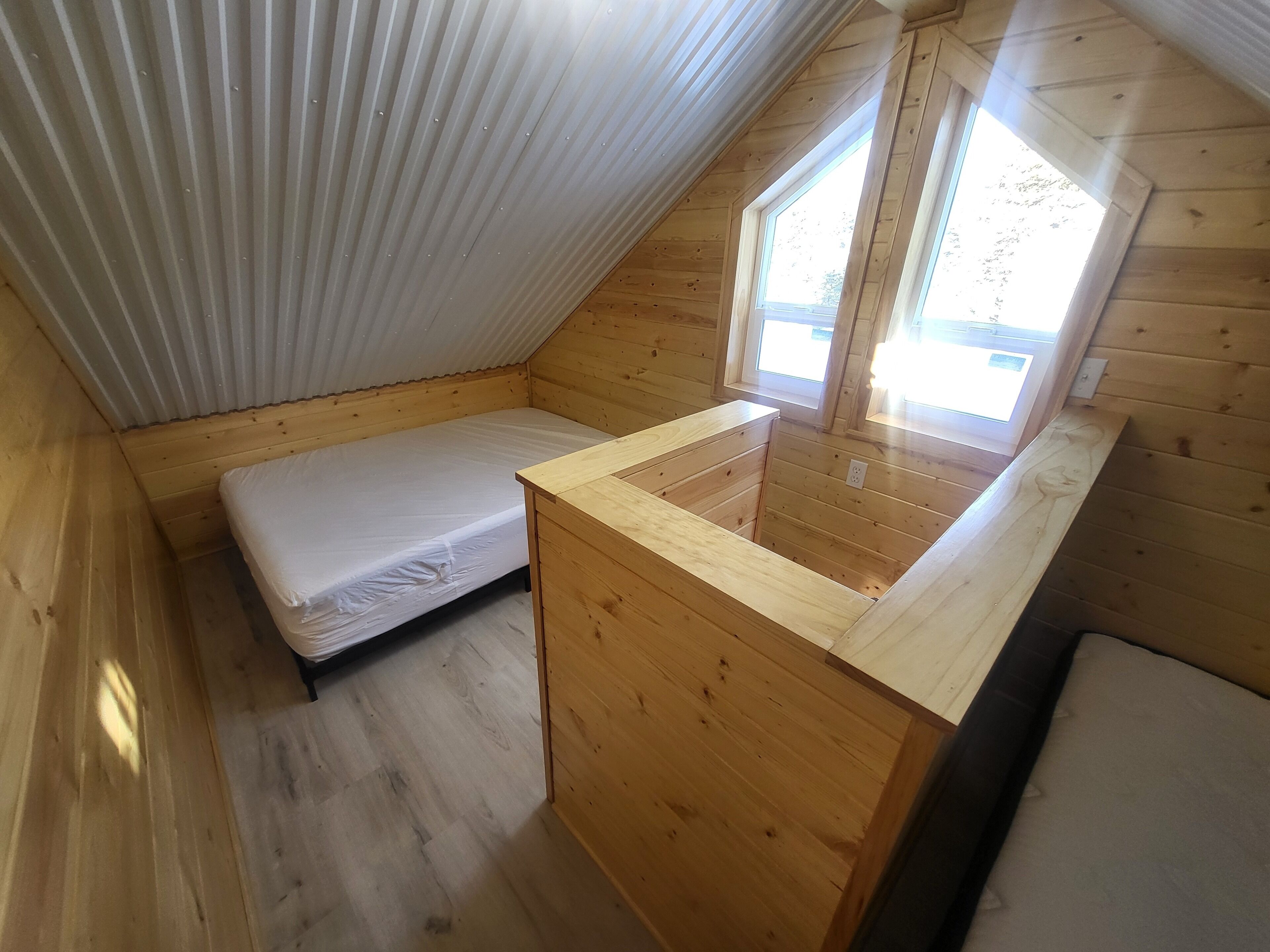 A small, wooden cabin with a sloped ceiling, a single bed, a wooden desk, and a window.