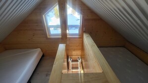 A small attic bedroom with a skylight, wooden walls, and a loft bed.