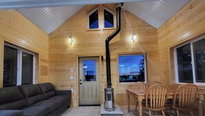 A cozy cabin interior with a sofa, dining table, chairs, a chimney, and large windows.
