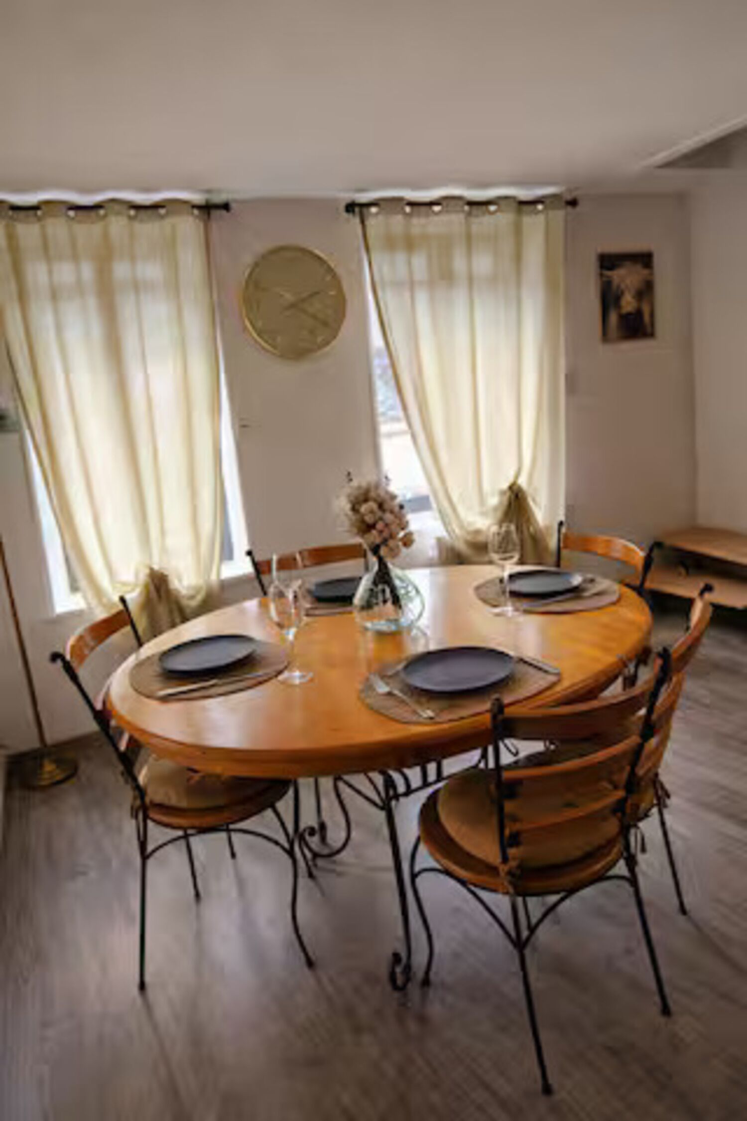 Ein Esszimmer mit einem runden Holztisch, vier Stühlen, einer Blumenvase und einer Uhr an der Wand.