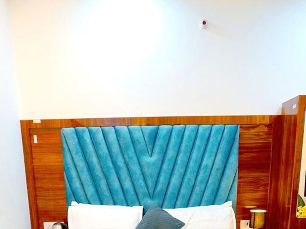 Een slaapkamer met een houten hoofdbord, een bed met witte beddengoed en een klein nachtkastje met een lamp.