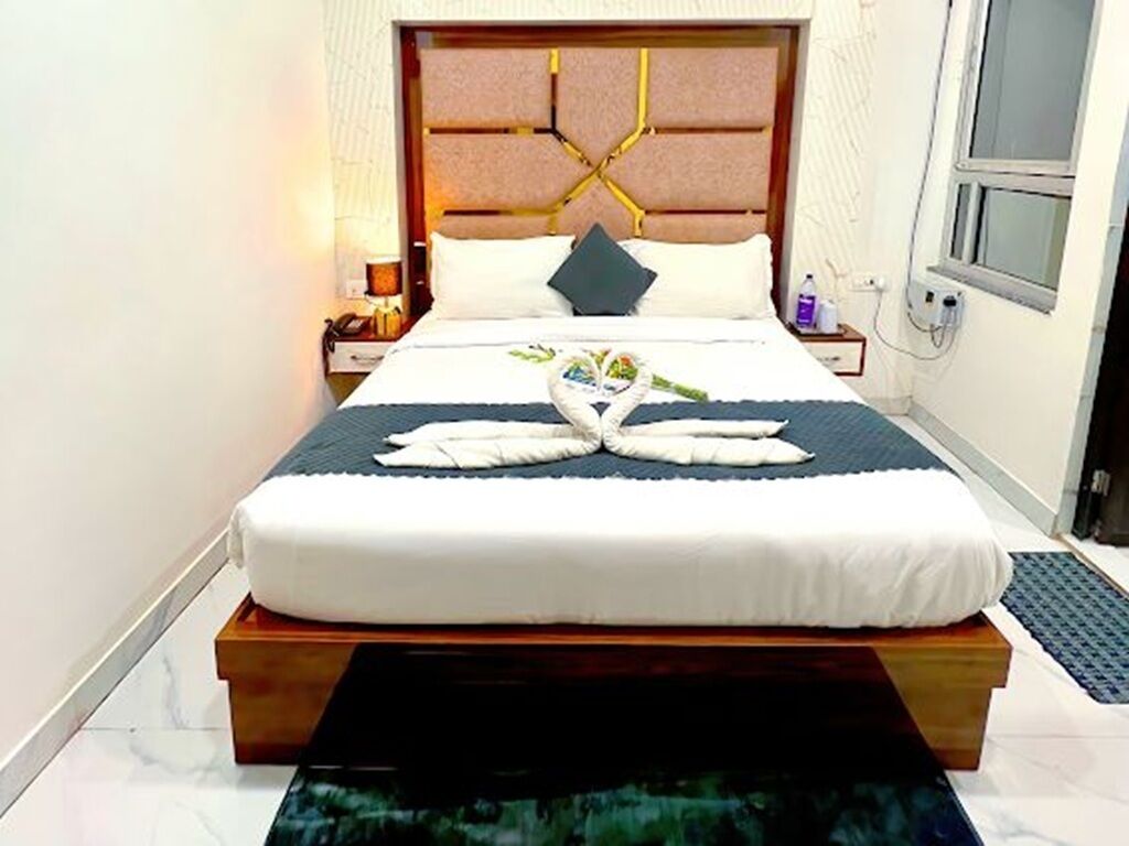 A neatly made bed with a headboard, a bedside table with a lamp, and a window.