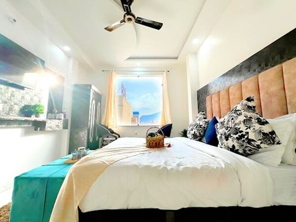 A hotel room with a bed, a ceiling fan, a window with a view, and a teal-colored table.