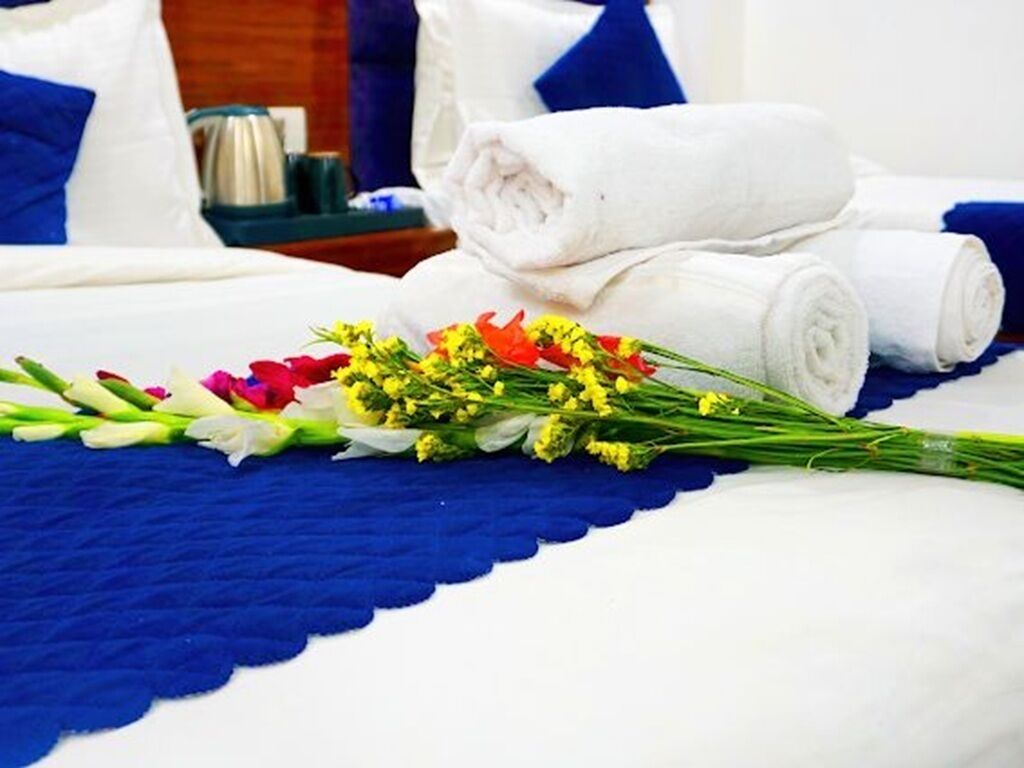 A neatly made bed with rolled white towels and a bouquet of flowers.