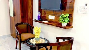 A room with a wooden wardrobe, a television mounted on the wall, a small table with a vase of flowers, and a chair. - Asha heritage Hotel & Restro (Haridwar)