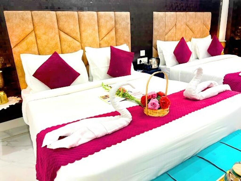 Une chambre d’hôtel avec deux lits, chacun doté d’une tête de lit, de draps blancs et d’oreillers rouges. Un bouquet de fleurs est posé sur l’un des lits, et une corbeille contenant des serviettes se trouve à proximité.