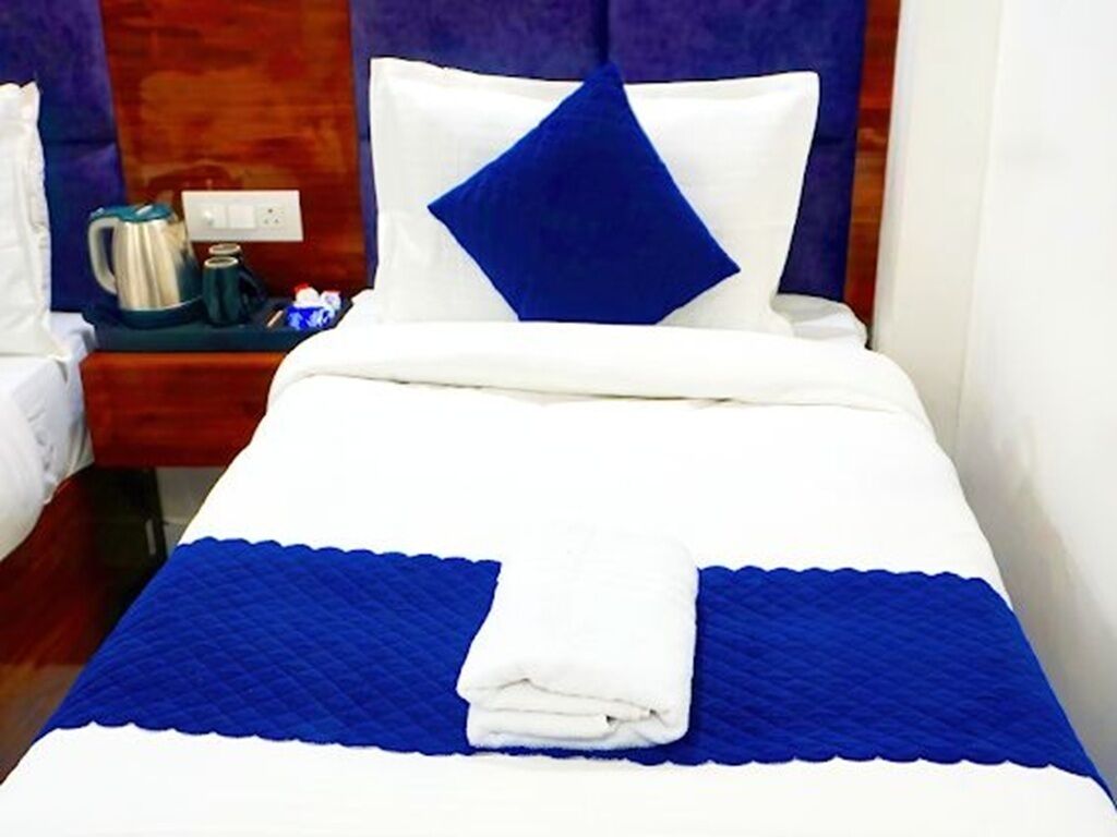 A hotel room with a neatly made bed, a nightstand with a kettle, and a power outlet.