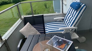 En balkon med en blå- og hvidstribet loungeseng, et lille bord og et magasin.
