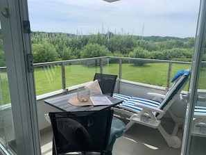 A balcony with a table, chairs, and a view of a green landscape.