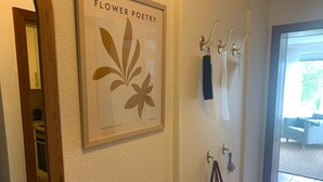 Et billede i ramme med titlen 'Flower Poetry' på en væg, et knagered med genstande, og en dør der fører til et rum.