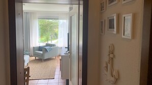 En døråbning ind til en stue med sofa, fjernsyn og udsigt til grønne omgivelser.