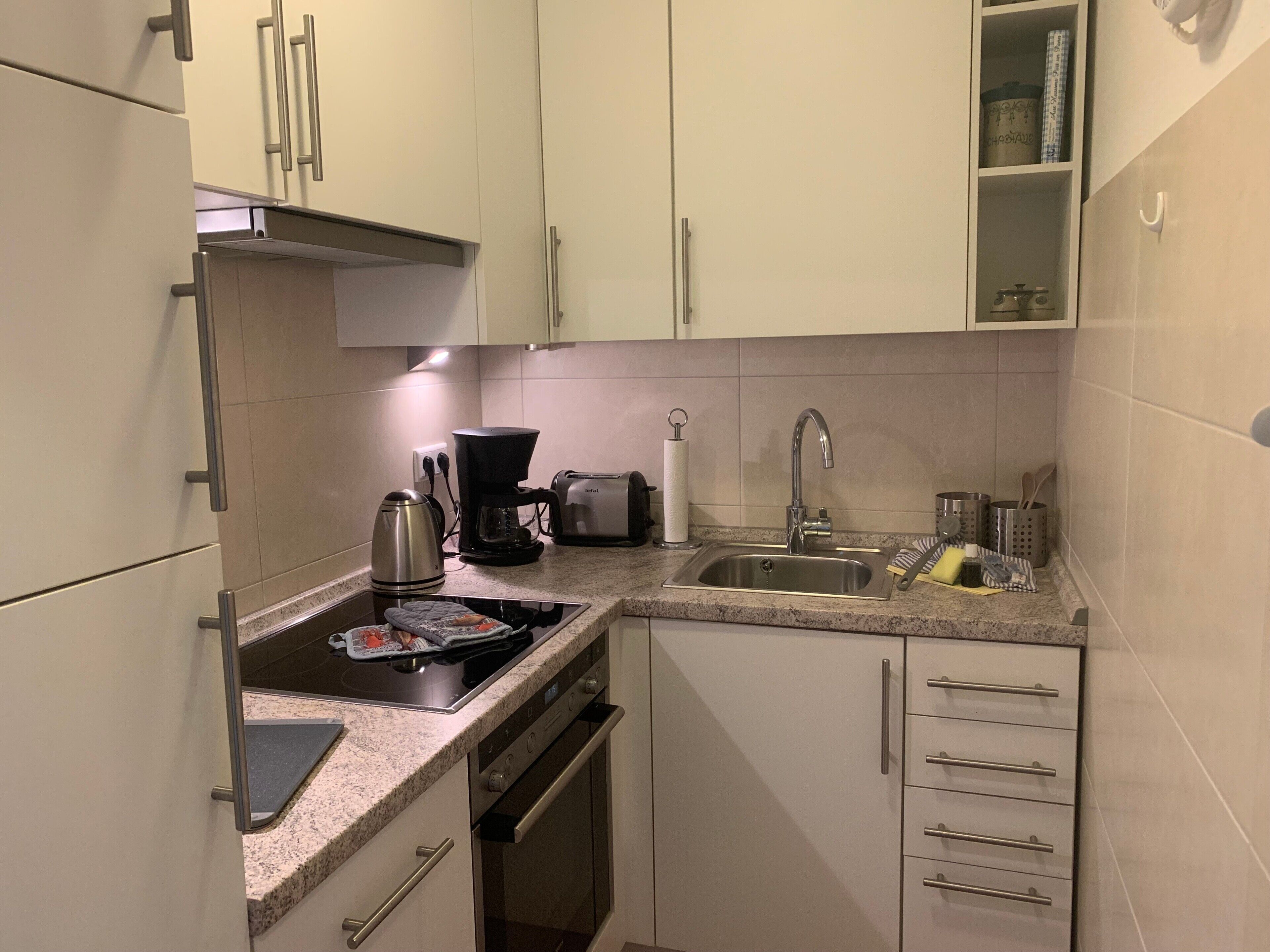 Una cocina compacta con estufa, cafetera y pileta.