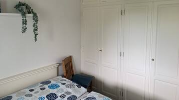 A bedroom with a bed, a wooden chair, a hanging plant, and a wardrobe.