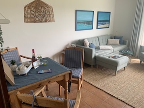 A living room with a dining table, chairs, a sofa, and two framed pictures on the wall.
