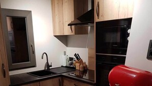 Kompakti keittiö, jossa on puiset kaapit, Bosch-uuni ja punainen grilli.