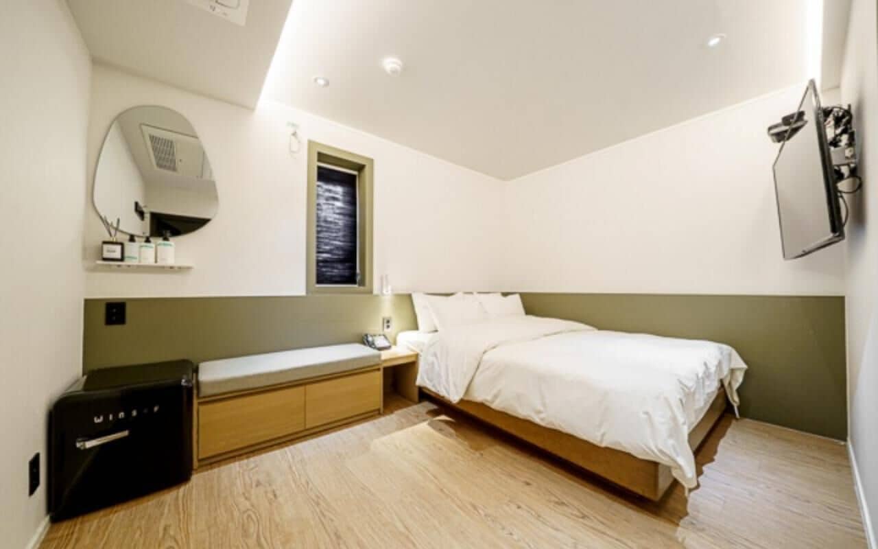 Un dormitorio con cama, mesita de noche, lámpara, espejo y un pequeño armario.