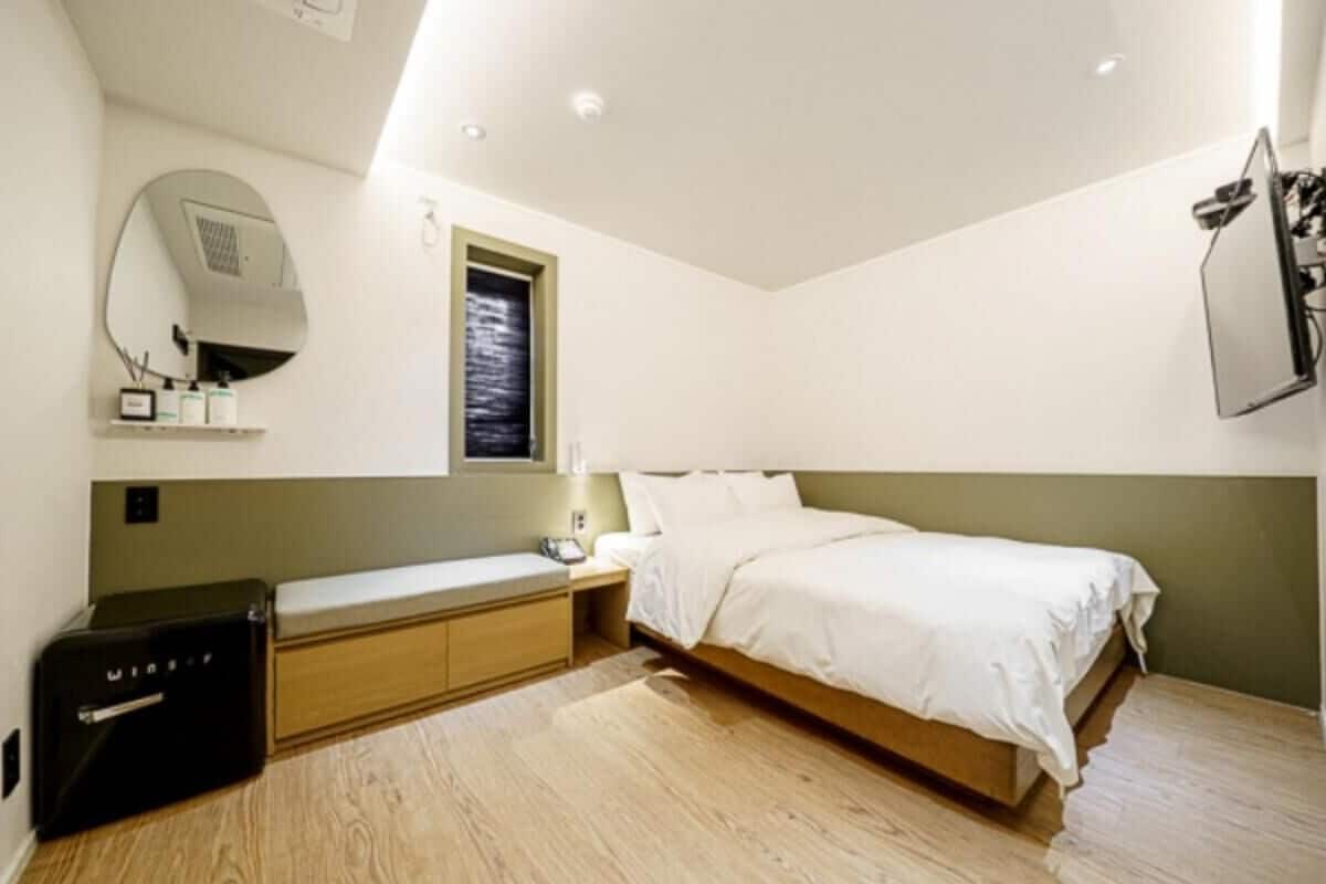 Ein Schlafzimmer mit Bett, Nachttisch, Lampe, Spiegel und einem kleinen Schrank.