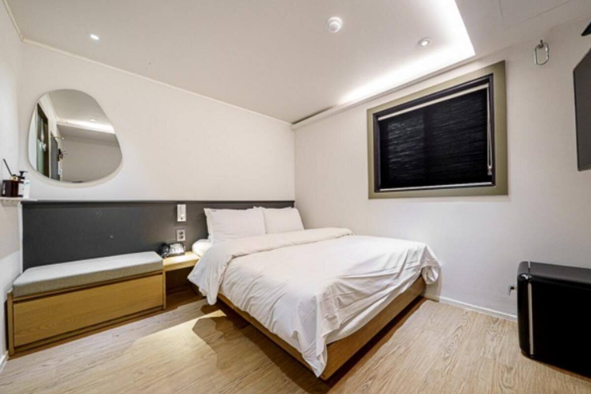 Ein Schlafzimmer mit einem Bett, einem Nachttisch, einer Bank und einem großen Fenster.