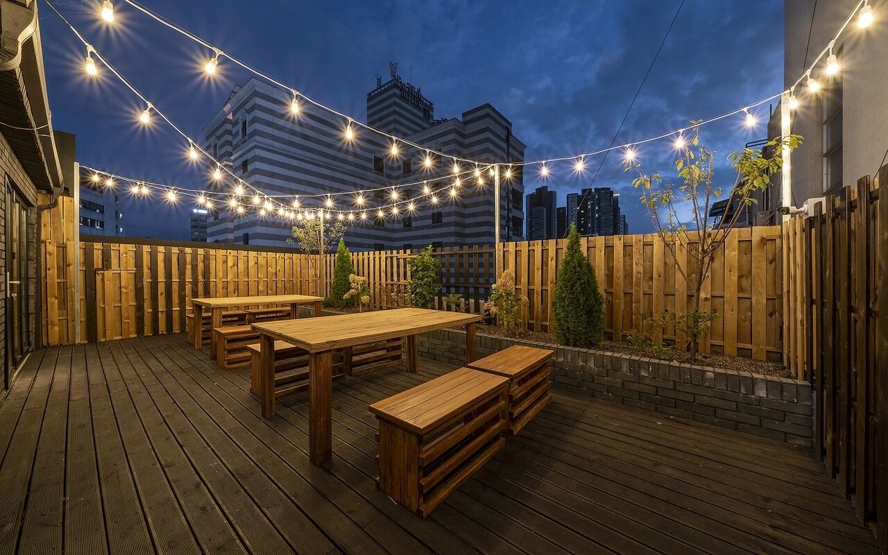 Una terraza al aire libre con mobiliario de madera y luces colgantes.