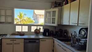 Uma cozinha com janela, escorredor de louça, cafeteira e máquina de lavar loiça.