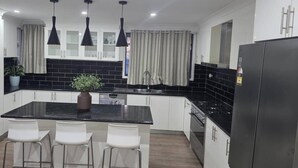 A modern kitchen with white cabinets, a black countertop, a central island with chairs, pendant lights, and a refrigerator. - Tranquil Oakhurst Retreat Your Peaceful Home Away from Home (Oakhurst)