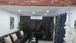 A living room with a black sofa, a flat-screen TV, a ceiling fan, and a brick wall. - Tranquil Oakhurst Retreat Your Peaceful Home Away from Home (Oakhurst)