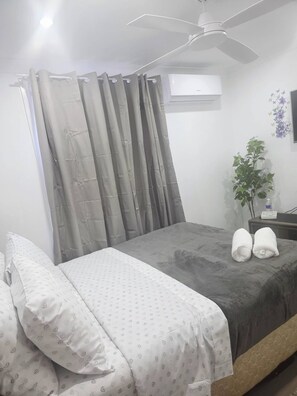 A hotel room with a bed, a bedside table with a bottle, a plant, and a ceiling fan. - Tranquil Oakhurst Retreat Your Peaceful Home Away from Home (Oakhurst)