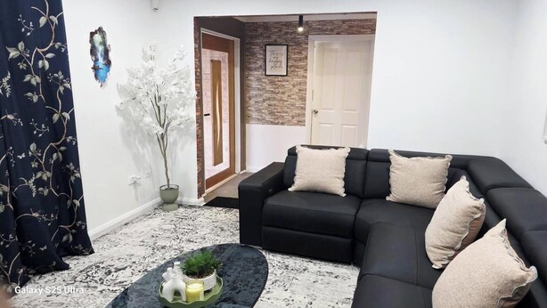A living room with a black sofa, decorative pillows, a small table with a plant, and a wall-mounted painting. - Tranquil Oakhurst Retreat Your Peaceful Home Away from Home (Oakhurst)