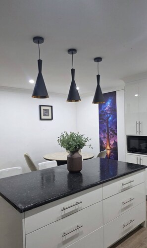 Une cuisine moderne avec un plan de travail noir, des armoires blanches et trois suspensions lumineuses.