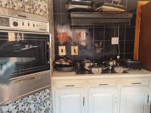 A kitchen with a built-in oven, a stove, and a microwave. There are cabinets and a countertop with pots and pans.