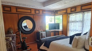 Ein Hotelzimmer mit einem großen Bett, einem runden Spiegel, einem Schreibtisch mit Fernseher und einem Fenster mit Vorhängen.