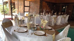 Una mesa de banquete dispuesta para un evento formal, con manteles blancos, detalles dorados y sillas adornadas con cintas blancas y doradas.