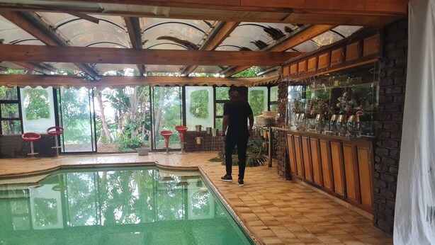 Una piscina interior con suelo de baldosas, una zona de bar con copas, y vistas a zonas verdes exteriores.