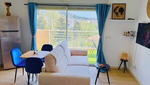 Una sala de estar moderna con un sofá, sillas, una mesa de comedor, un televisor y un balcón con vistas.