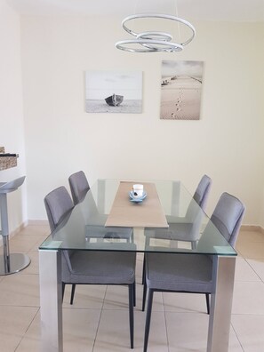 A modern dining area with a glass table, grey chairs, and a hanging light fixture. - 2BR Condo with Pool, Walk to Beach, Bávaro (Punta Cana)