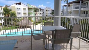 Ein Balkon mit Tisch und Stühlen, ein Schwimmbad und Gebäude im Hintergrund.