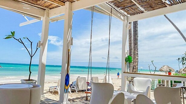 Ein Restaurant direkt am Strand mit Außenbereich, Blick auf das Meer und einer Palme.