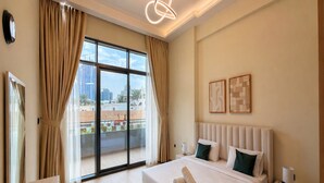 Ein Hotelzimmer mit einem großen Bett, einem Nachttisch, Vorhängen an einem Fenster und Blick auf Gebäude.