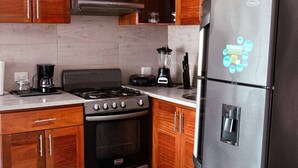 Una cucina compatta con mobili in legno, un frigorifero in acciaio inossidabile, un forno a microonde, un fornello e una lampada a sospensione.