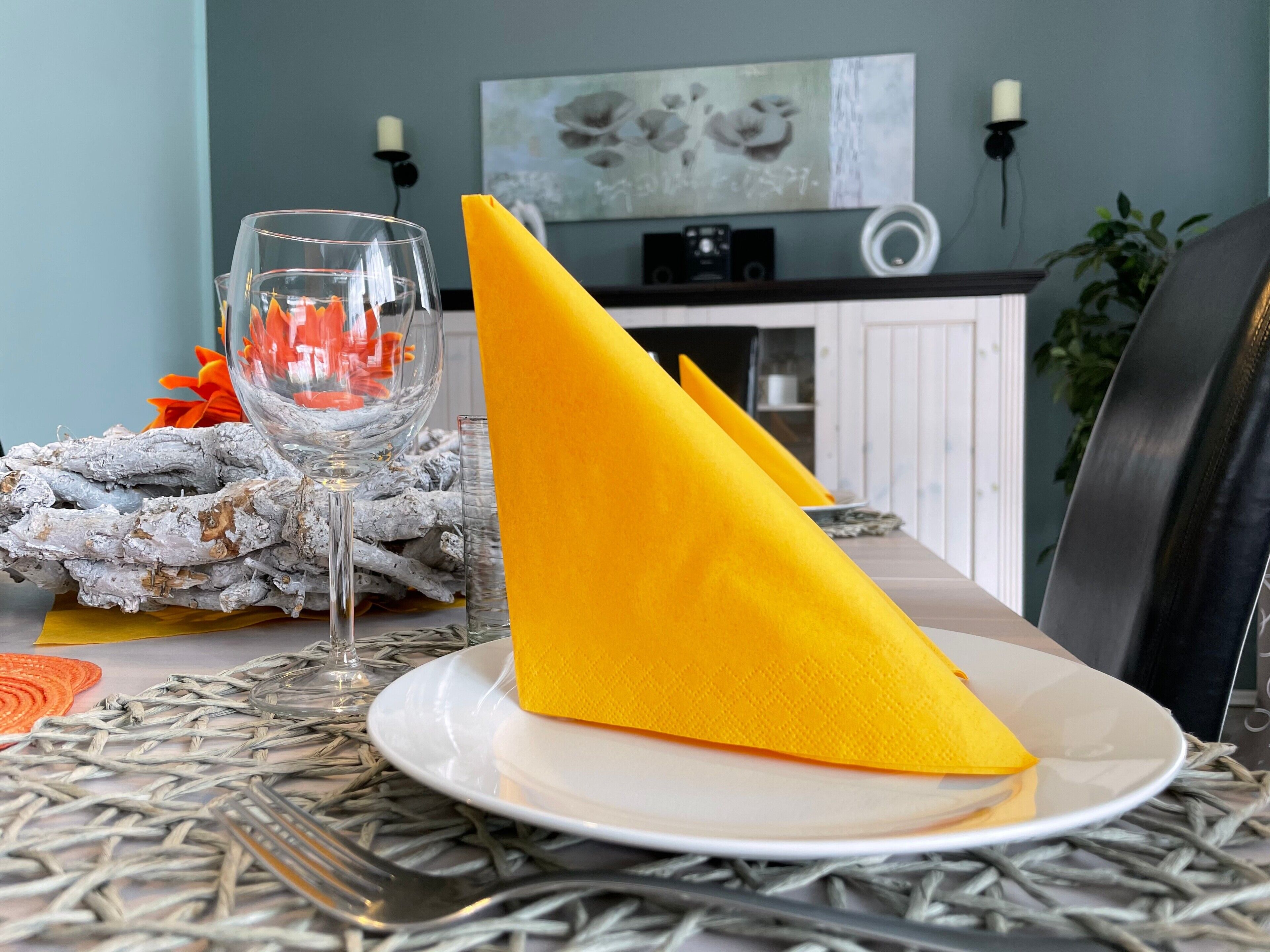A dining table with a white plate, a glass, and a yellow napkin.