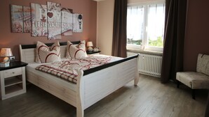 Un dormitorio con cama, mesitas de noche, una silla, una ventana con cortinas y un letrero en la pared que dice 'HOME'.