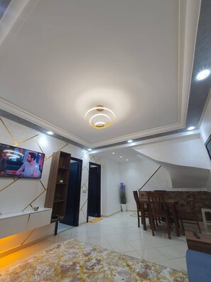 A modern living room with a TV, a dining area, and a decorative ceiling light. - Superb Duplex in the center of Tangier (Tangier)