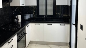 Eine kompakte Küche mit weißen Schränken, einer schwarzen Arbeitsplatte, einem eingebauten Backofen und einer Pendelleuchte.