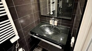 A bathroom with a black sink, a mirror, a towel rack, and a light fixture. - Charming studio in the heart of République (Paris)