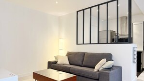 A modern living room with a grey sofa, a glass coffee table, and a large mirror on the wall. - Charming studio in the heart of République (Paris)