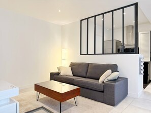 A modern living room with a grey sofa, a glass coffee table, and a large mirror on the wall. - Charming studio in the heart of République (Paris)
