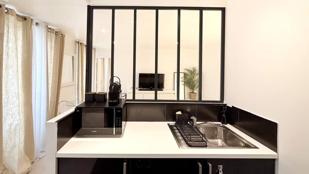 A modern kitchen with a built-in stove, a sink, and a flat-screen TV mounted on the wall. - Charming studio in the heart of République (Paris)