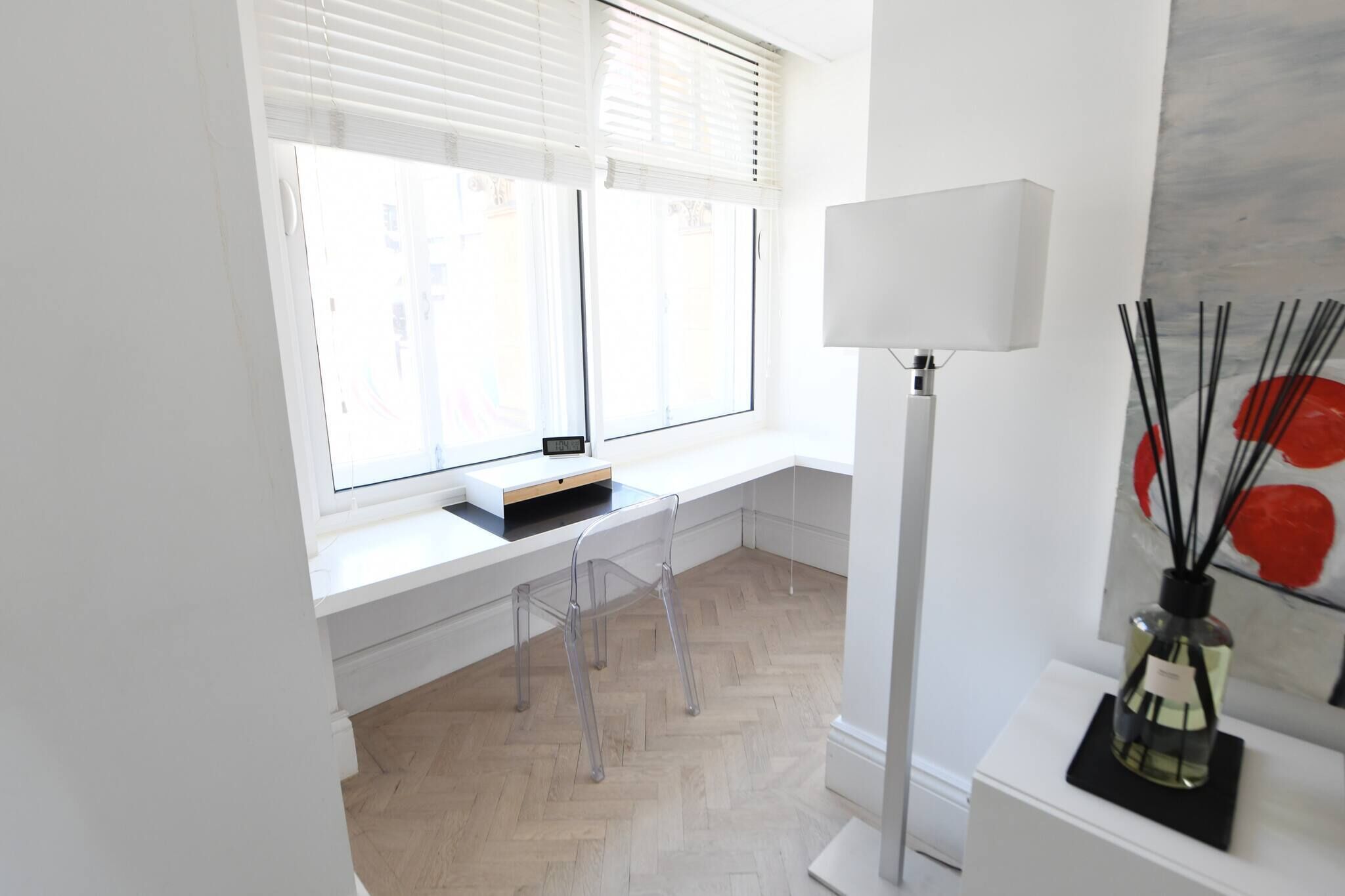 A bright room with a desk, a chair, a lamp, and a window with blinds.