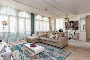 Ein modernes Wohnzimmer mit Ecksofa, Couchtisch und großem Fenster mit Jalousien.