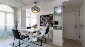 Un comedor moderno con una mesa blanca, sillas negras, una lámpara colgante y un cuadro grande en la pared.